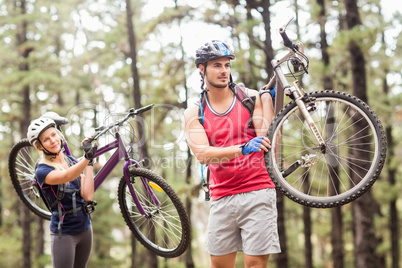 Young happy couple on bikes looking away carrying bikes