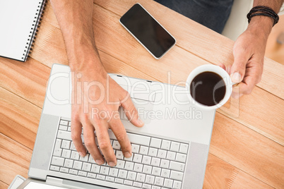 Hands holding coffee cup and typing on laptop