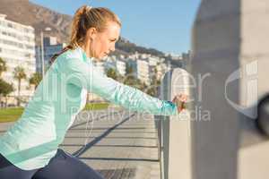 Fit blonde stretching on railing and listening to music