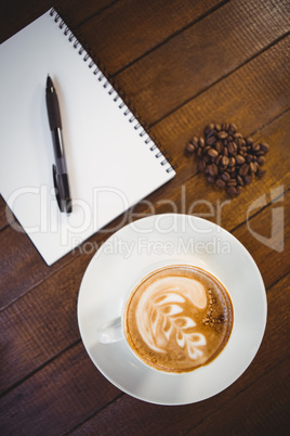 Cup of cappuccino with coffee art and notepad