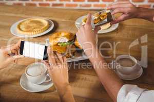 Two people taking picture of foods