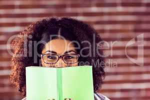 Attractive smiling hipster hiding behind book