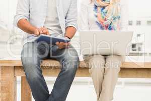 Casual designers sitting on wooden desk and using devices