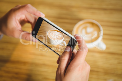 Man photographing his cappuccino with coffee art