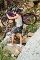 Athletic brunette carrying her mountain bike over stream