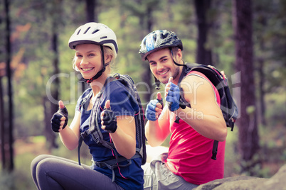 Young happy biker couple sitting on a rock looking at the camera