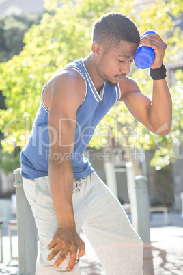 An handsome athlete leaning a bottle against his head