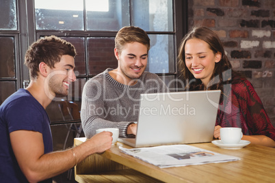 Smiling friends having coffee together and looking at laptop