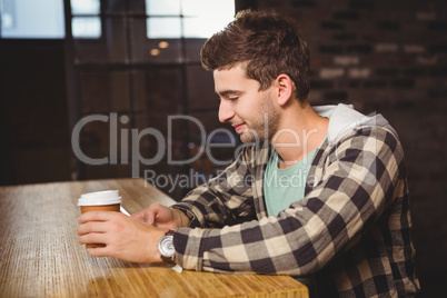 Smiling hipster texting and holding take-away cup