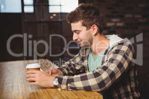 Smiling hipster texting and holding take-away cup