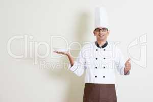 Handsome Indian male chef in uniform holding a plate and thumb u