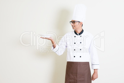 Handsome Indian male chef in uniform holding an empty plate