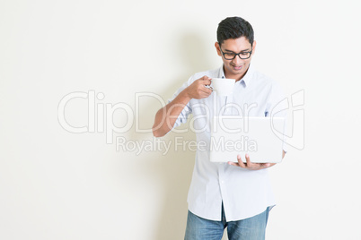 Casual business Indian male using laptop and drinking coffee