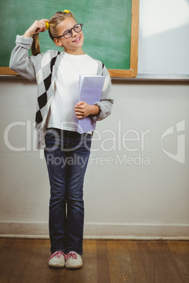 Cute pupil thinking and holding books in a classroom