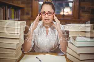 Focused blonde teacher sitting between books in the library