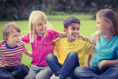 Smiling classmates talking and sitting in grass