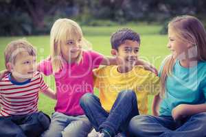 Smiling classmates talking and sitting in grass