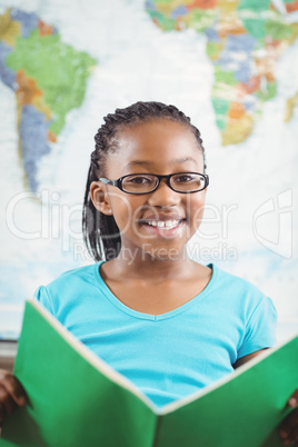Smiling pupil reading book in a classroom