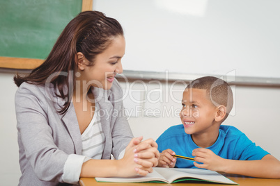 Pretty teacher helping pupil at his desk