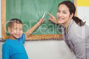 Pretty teacher helping pupil at chalkboard