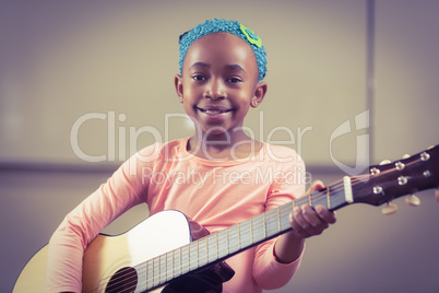 Smiling pupil playing guitar in a classroom