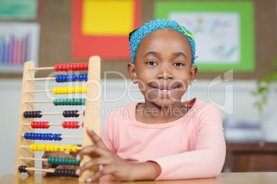 Smiling pupil calculating with abacus in a classroom