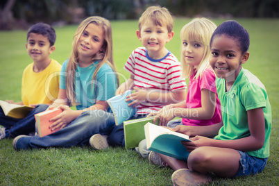 Smiling classmates sitting in grass and holding books