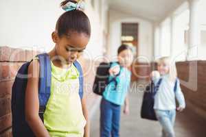 Sad pupil being bullied by classmates at corridor