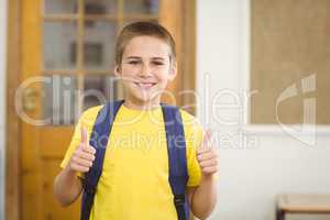 Smiling pupil with schoolbag doing thumbs up in a classroom