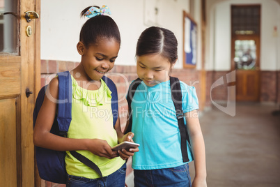 Cute pupils looking at smartphone at corridor