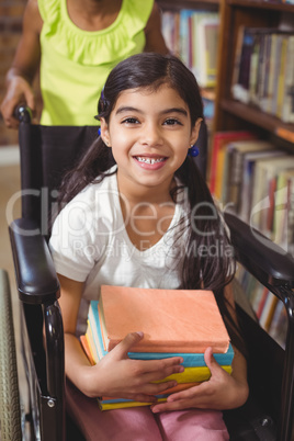 Smiling pupil in wheelchair holding books in the library