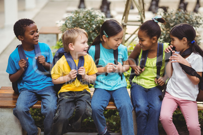 Happy pupils with schoolbags sitting on bench