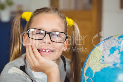 Cute pupil smiling next to globe in a classroom