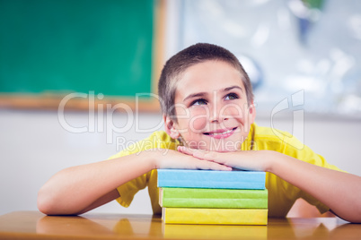 Smiling pupil leaning on pile of books in a classroom