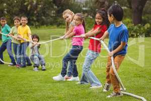 Cute pupils playing tug of war on the grass outside