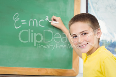 Smiling pupil writing on chalkboard in a classroom