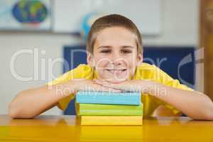 Smiling pupil leaning on pile of books in a classroom