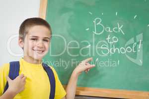 Smiling pupil pointing on back to school sign on chalkboard