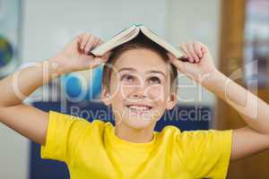 Smiling pupil holding book on head in a classroom