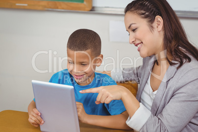Pretty teacher and pupil using tablet at his desk
