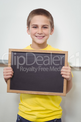 Smiling pupil holding chalkboard in a classroom