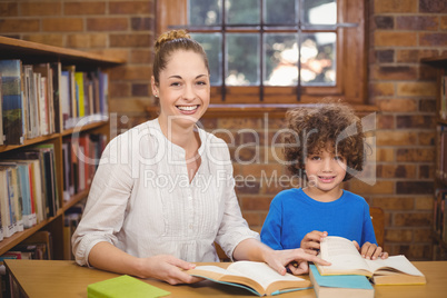Blonde teacher and pupil reading books in the library