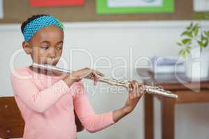 Cute pupil playing flute in a classroom