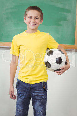 Smiling pupil holding football in a classroom