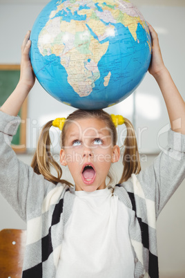 Cute pupil balancing globe on head in a classroom