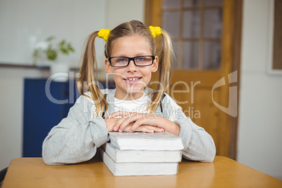 Cute pupil leaning on pile of books in a classroom