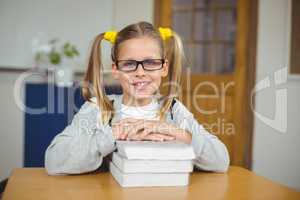 Cute pupil leaning on pile of books in a classroom