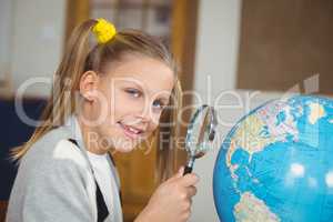 Cute pupil looking at globe through magnifier