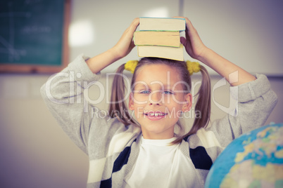 Cute pupil balancing books on head in a classroom