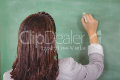 Rear view of teacher writing on chalkboard in a classroom